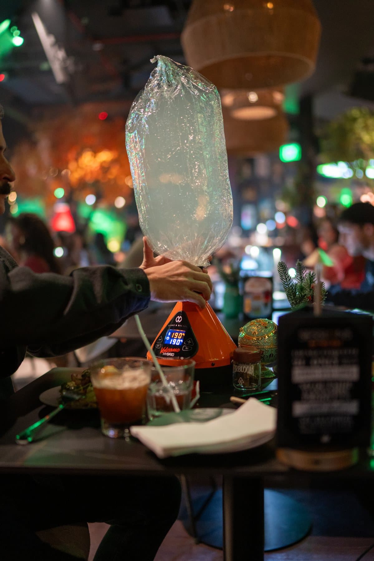 A guest holding up a filled vapor bag at a table set with mocktails
