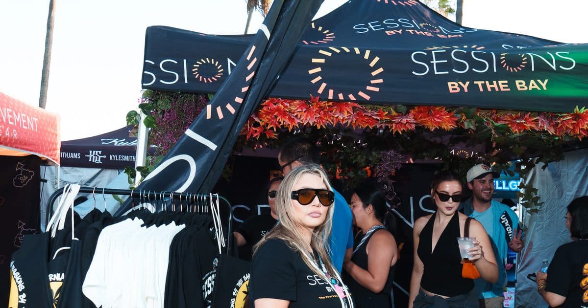 The Sessions By The Bay booth at Mission Bayfest 2026: a black canopy with the Sessions logo, trimmed in orange leaves, over a rack of Sessions hoodies and tees